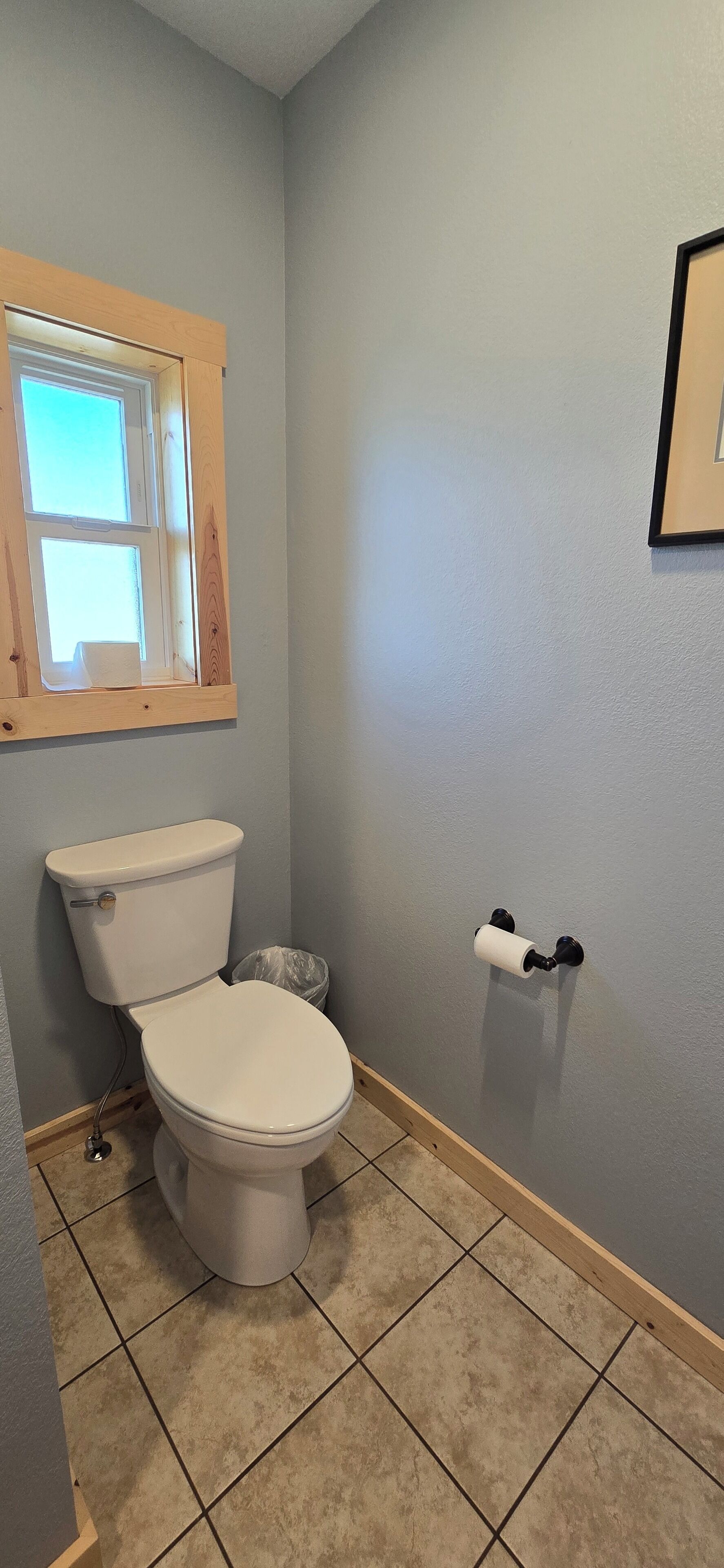 Un baño con un inodoro, una ventana y un portaescobillas en la pared.