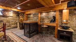 Un interior rústico con pared de piedra, vigas de madera, chimenea y zona de bar.