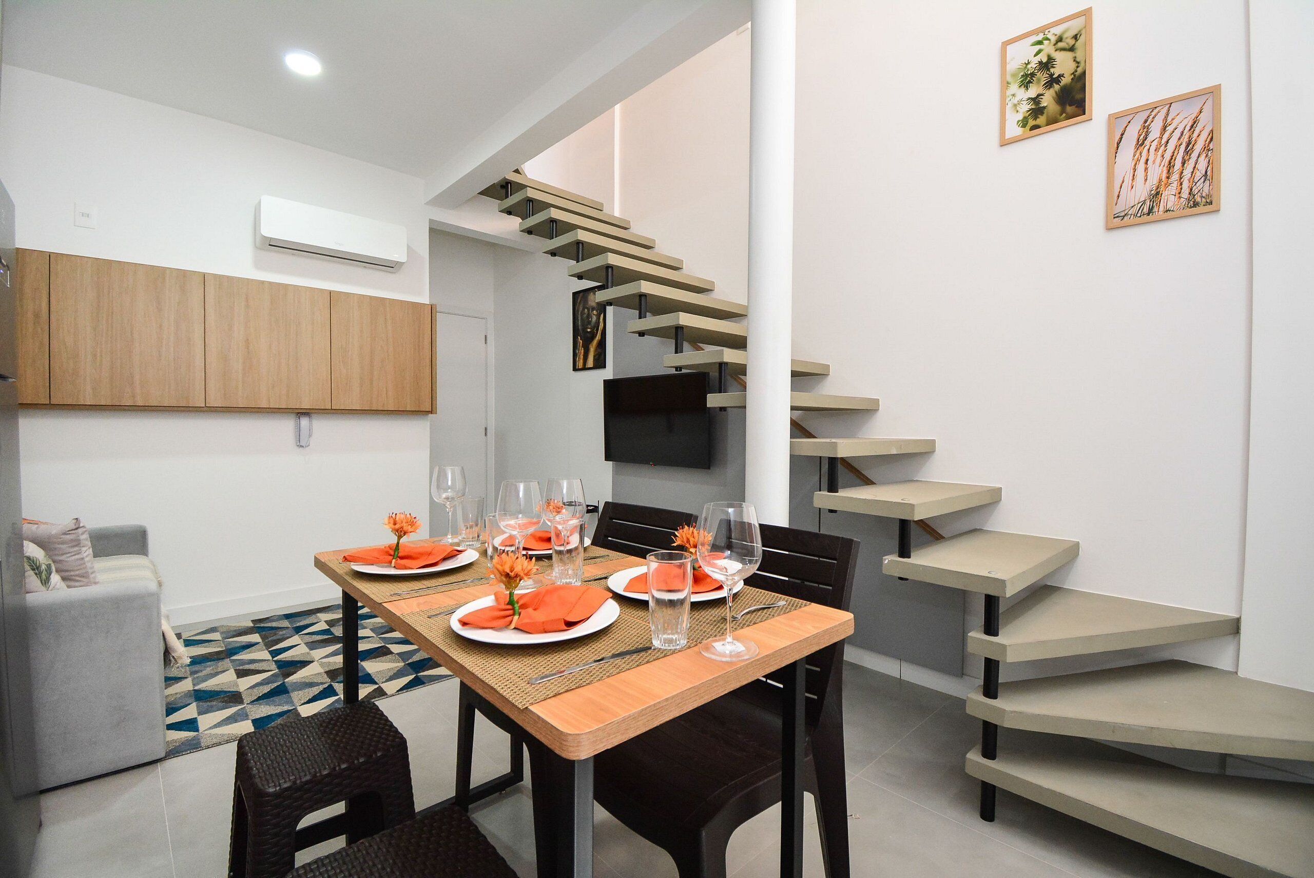 Une cuisine moderne dotée d’un four encastré, un coin repas avec une table en bois prévue pour quatre personnes, et un escalier au design original.