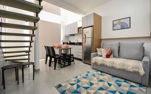 A modern kitchen with a built-in refrigerator, dining area with chairs and a table, and a grey sofa with cushions.