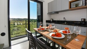 A dining area with a view of a green landscape through large windows, a wooden table set for two, and modern kitchen cabinets. - Loft - Haleiwa Novo Campeche (Florianopolis)