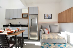 A compact kitchen with grey cabinets, a stainless steel refrigerator, and a dining area with a table set for two.