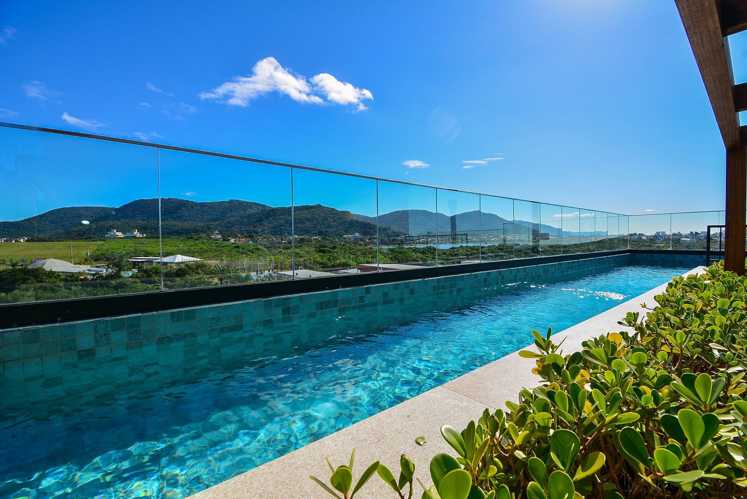 Una piscina azul cristalina con una barrera de vidrio, rodeada de vegetación y con vistas a un paisaje montañoso.