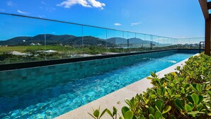Ein klares, blaues Schwimmbecken mit Glastrennwand, umgeben von Grün und mit Blick auf eine Berglandschaft.