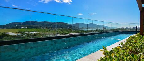 Una piscina azul cristalina con una barrera de vidrio, rodeada de vegetación y con vistas a un paisaje montañoso.