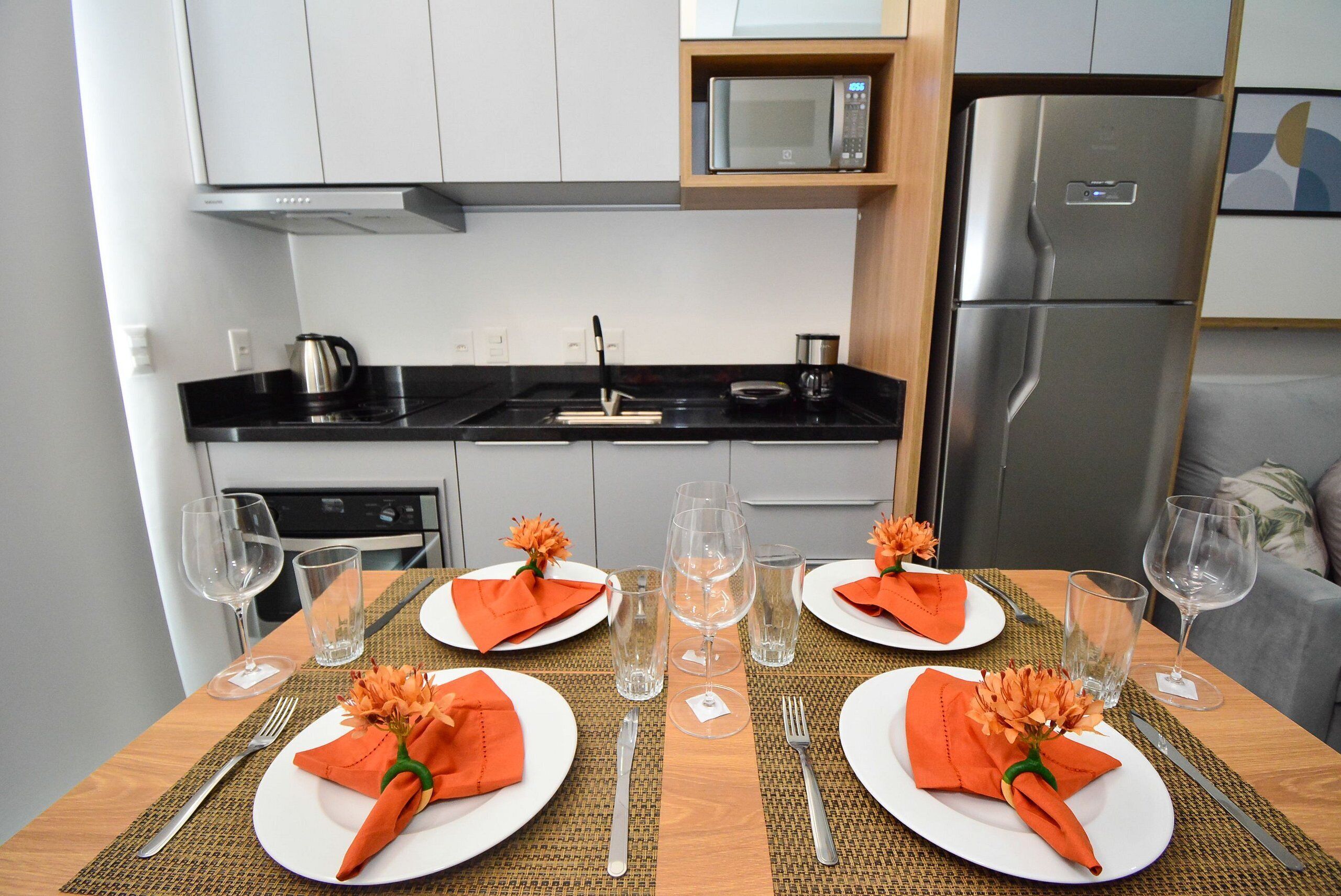 Une table à manger dressée pour deux personnes, avec des assiettes blanches, des serviettes orange et des verres transparents.
