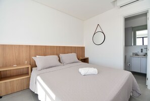 Un dormitorio moderno con cabecera de madera, un espejo redondo, una mesita de noche y una cama bien hecha con una toalla doblada.
