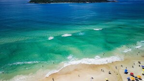 Ein Strand mit klarem türkisblauem Wasser, einem sandigen Ufer und einer kleinen Insel in der Ferne.