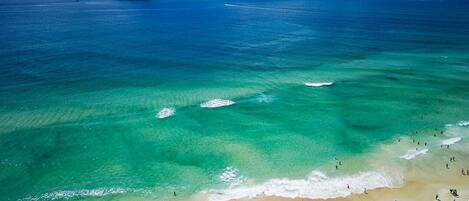 A beach with clear turquoise waters, a sandy shore, and a small island in the distance.