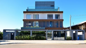 A modern multi-story building with a flat roof, large windows, and a covered entrance area. - Loft - Haleiwa Novo Campeche (Florianopolis)