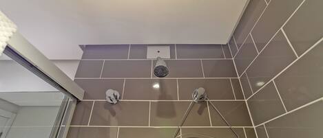 A corner of a bathroom with a shower, a towel rack, and a wall-mounted light fixture.