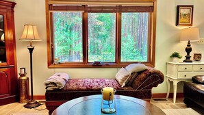 A cozy room with a bed, a round table with a candle, a lamp, and a window with a forest view.