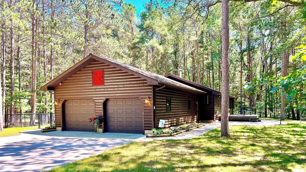 A wooden cabin with a garage, surrounded by a forest.