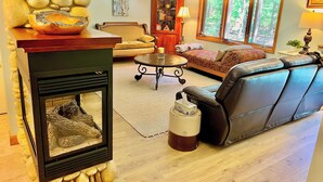 A living room with a stone fireplace, leather sofa, and a large window with a view of trees.