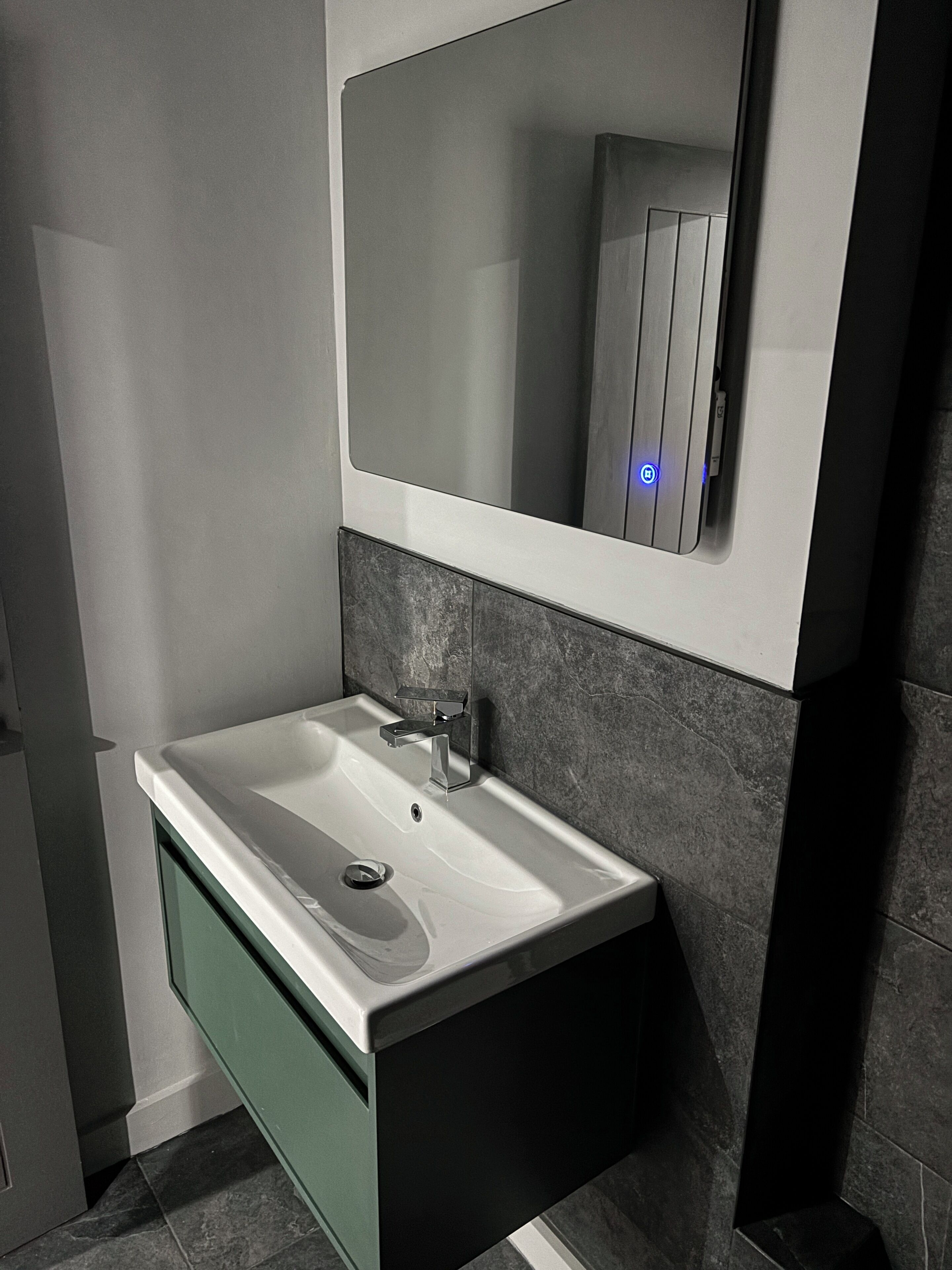 Un baño moderno con un lavabo blanco, un espejo y paredes de azulejos oscuros.