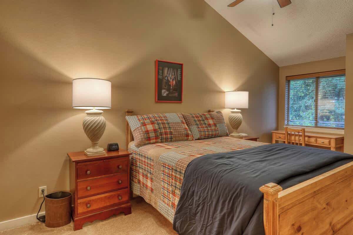 Une chambre à coucher comprenant un lit, deux tables de chevet, une commode, une fenêtre avec des stores et un ventilateur de plafond.