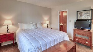 A bedroom with a large bed, two bedside tables with lamps, a wooden dresser with a television, and a door leading to another room. - Walk to Shops & Trails | Deck | A/C Condo (Pagosa Springs)