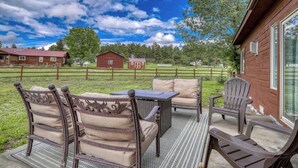 A patio with a table and chairs, a wooden deck, and a view of a rural landscape with barns. - Pet-Friendly Retreat w/ Fenced Yard & Fire Pit (Pagosa Springs)