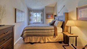 A bedroom with a large bed, a nightstand, a dresser, and a window with curtains.