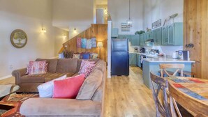 A cozy living room with a brown sofa, a wooden dining table, and a kitchen in the background.