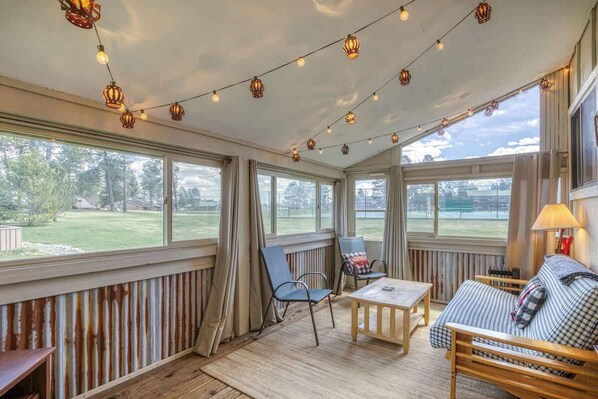 A cozy room with a wooden bench, a sofa, and a table. There are curtains on the windows, and string lights hang from the ceiling. - Bright Townhouse with Sunroom & AC Near Lakes (Pagosa Springs)