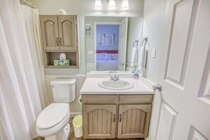 A compact bathroom with a toilet, sink, and wooden cabinets. - Bright Townhouse with Sunroom & AC Near Lakes (Pagosa Springs)