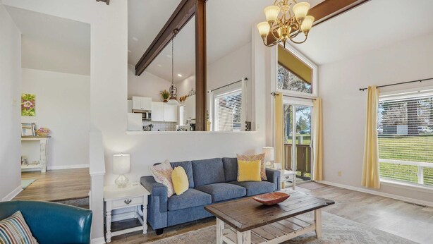 A spacious living room with a blue sofa, a wooden coffee table, and a view of a garden through large windows. - Bright 2BR End Unit | A/C + Walkable Location (Pagosa Springs)