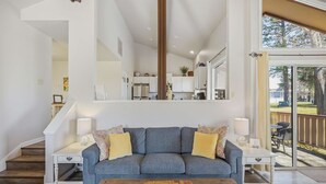 A living room with a blue sofa, two side tables with lamps, a wooden coffee table, and a view of the kitchen and outdoor area through a glass door. - Bright 2BR End Unit | A/C + Walkable Location (Pagosa Springs)