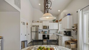 A kitchen with white cabinets, a central island with fruit, a hanging light fixture, and a window with blinds. - Bright 2BR End Unit | A/C + Walkable Location (Pagosa Springs)
