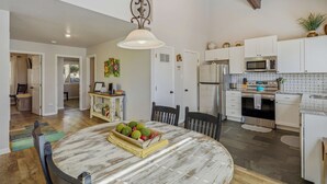 A spacious kitchen with white cabinets, a microwave, and a large dining table with a fruit centerpiece. - Bright 2BR End Unit | A/C + Walkable Location (Pagosa Springs)