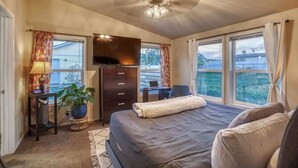 Een slaapkamer met een bed, een bureau, een televisie en een raam met gordijnen.
