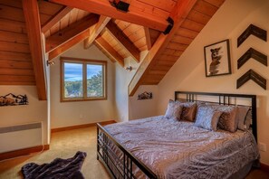 A bedroom with a sloped ceiling, a large window, a bed with patterned bedding, and wall decorations including a framed picture and chevron designs.