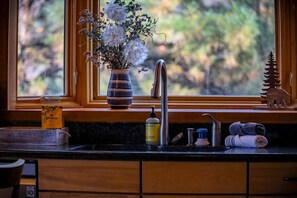 A kitchen with a window, a vase with flowers, a soap dispenser, and towels.