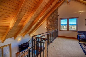 A spacious loft with a high ceiling, a stone wall, a staircase, a sofa, and a view through large windows.