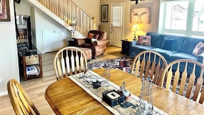 Un salon avec un escalier en bois, un canapé bleu, une table à manger avec des chaises et un tapis.