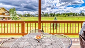 Un espace extérieur abrité, avec une table et des chaises en métal, une bouteille de vin et une vue sur un paysage verdoyant, délimité par une clôture en bois.