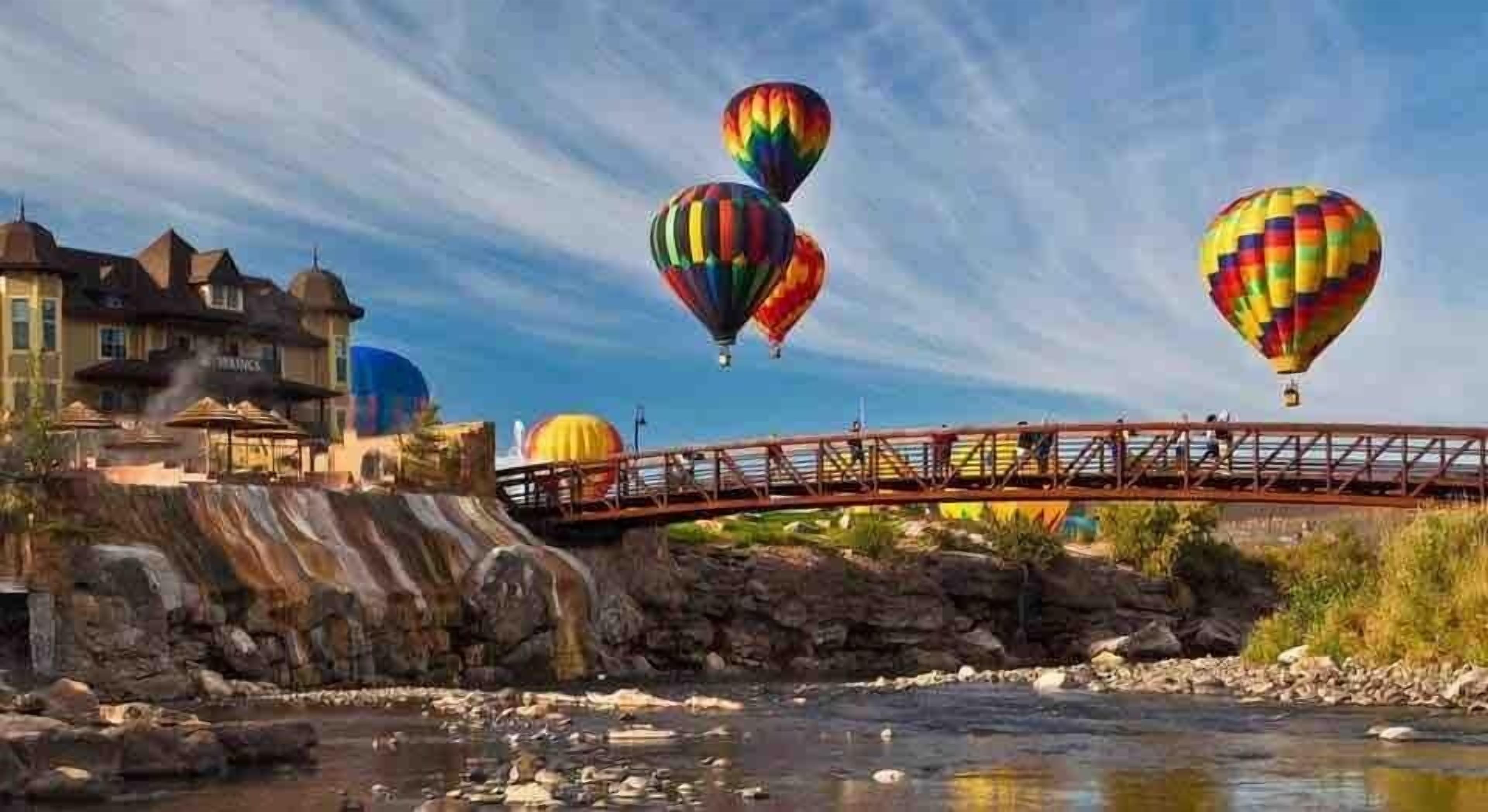 Een brug over een rivier met luchtballonnen op de achtergrond.