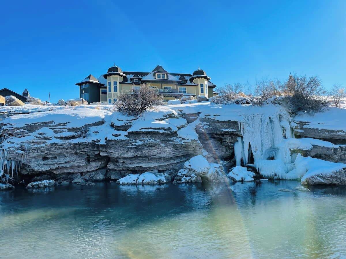 A large house with a prominent rock formation in front, surrounded by snow.