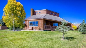 A two-story wooden house with a metal roof, large windows, and a covered porch.