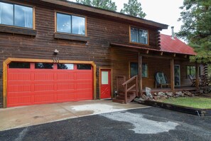 A two-story log cabin with a red garage door, a covered porch with outdoor seating, and a stone foundation.