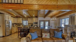 A spacious living room with a brown leather sofa, wooden ceiling beams, and a stone fireplace. - Golf Course Hot Tub Cabin with Wildlife Views (Pagosa Springs)