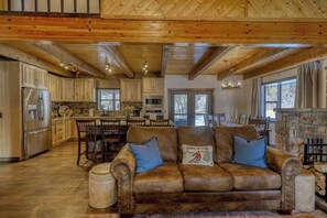 A spacious living room with a brown leather sofa, wooden ceiling beams, and a stone fireplace.