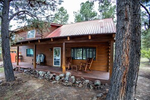 A rustic cabin with a wooden exterior, a porch with seating, and a stone wall foundation.