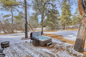 A hot tub set up outdoors with a wooden deck, surrounded by trees and a snowy landscape.