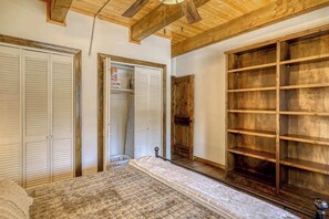 A bedroom with a bed, wooden shelves, a wardrobe, and a door leading to another room. - Golf Course Hot Tub Cabin with Wildlife Views (Pagosa Springs)
