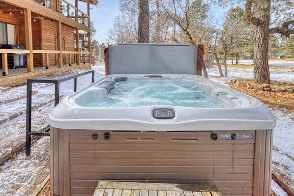 A hot tub in a snowy outdoor setting with a wooden deck and a building in the background. - Golf Course Hot Tub Cabin with Wildlife Views (Pagosa Springs)