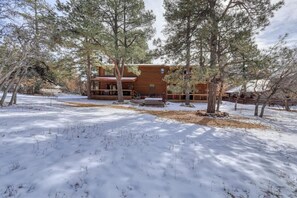 Una cabaña de madera rodeada de árboles y suelo cubierto de nieve.