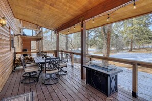 A wooden deck with a table and chairs, a fireplace, and a view of a snowy landscape.