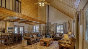A spacious living room with a high ceiling, wooden beams, a fireplace, and a cozy seating area with a coffee table and lamps. - Golf Course Hot Tub Cabin with Wildlife Views (Pagosa Springs)