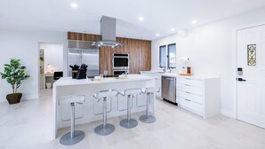 A modern kitchen with a central island, bar stools, stainless steel appliances, and a wooden accent wall.